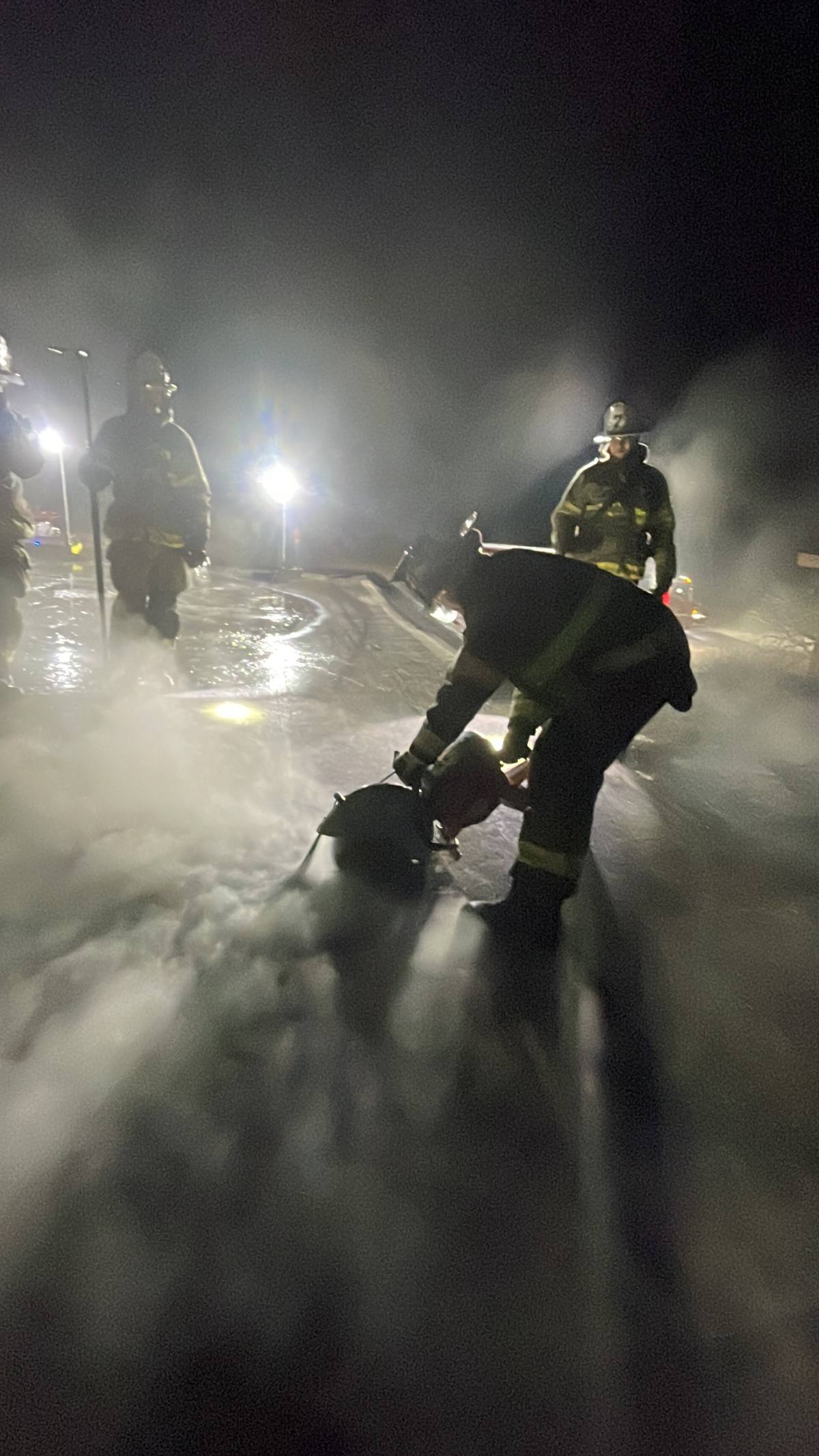 Firefighters working in heavy smoke under scene lighting at night