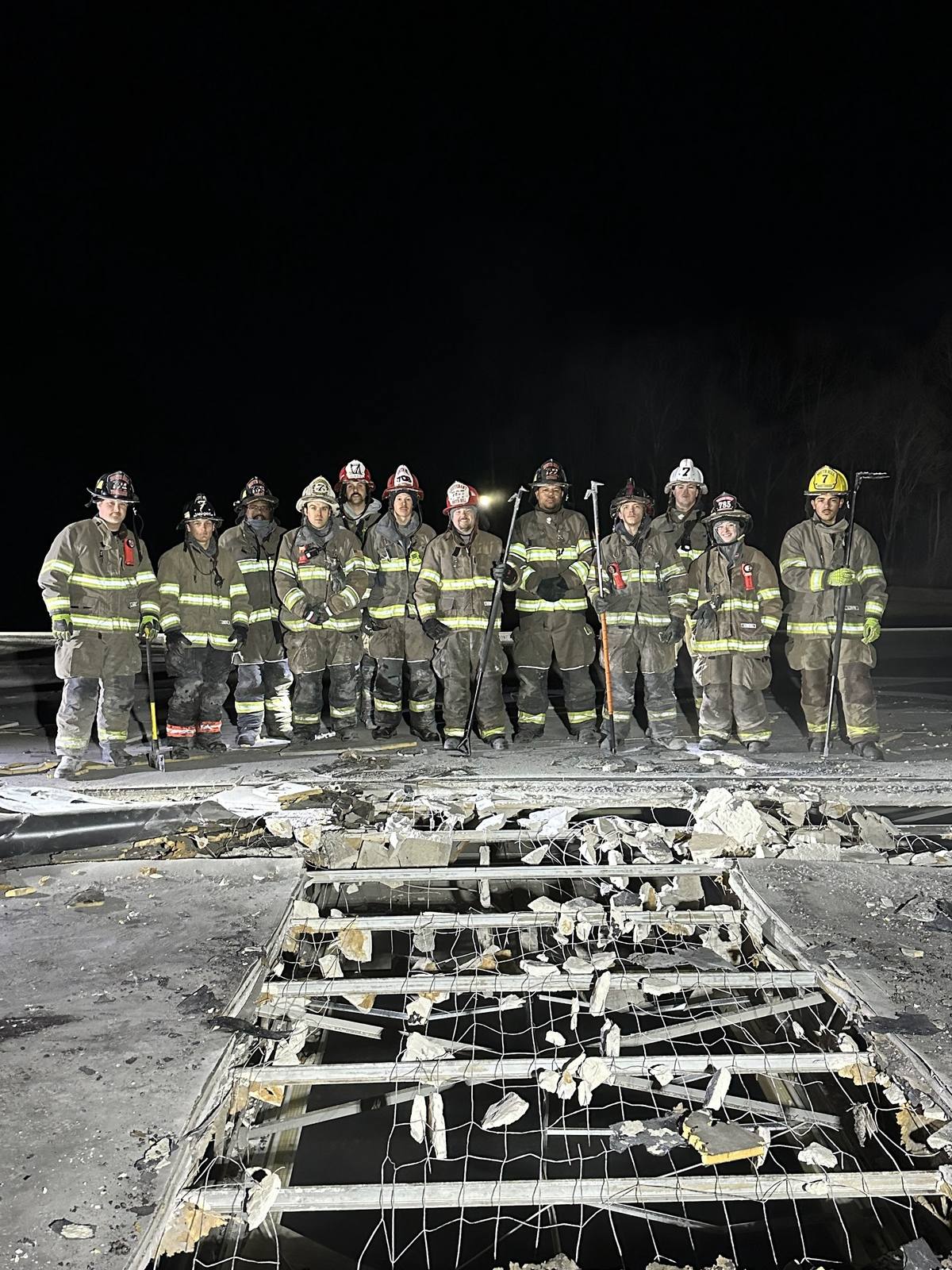 Night crew photograph after a fire, standing behind the collapsed roof structure