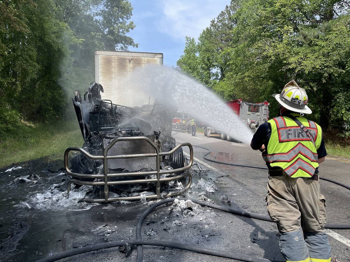 Firefighter flowing water on the remains of a burned tractor trailer