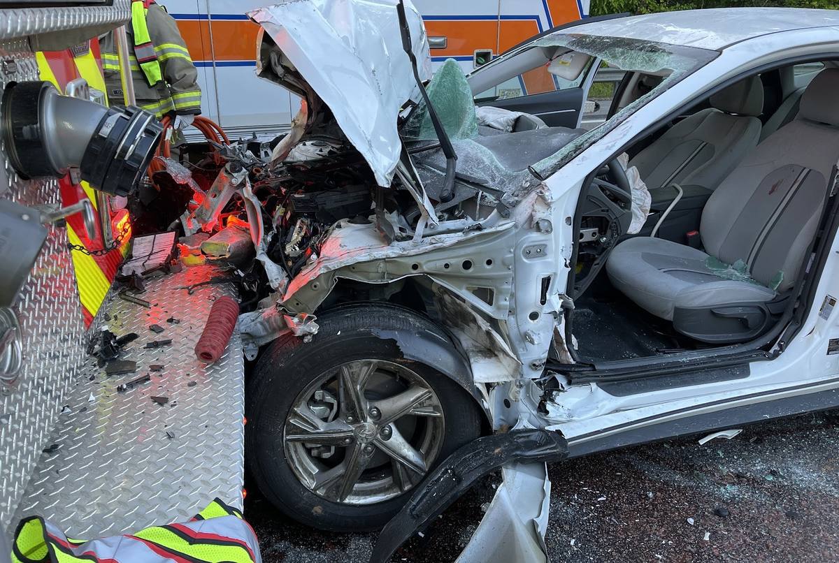 Extrication tools laid out against the crushed front of a sedan at a highway crash