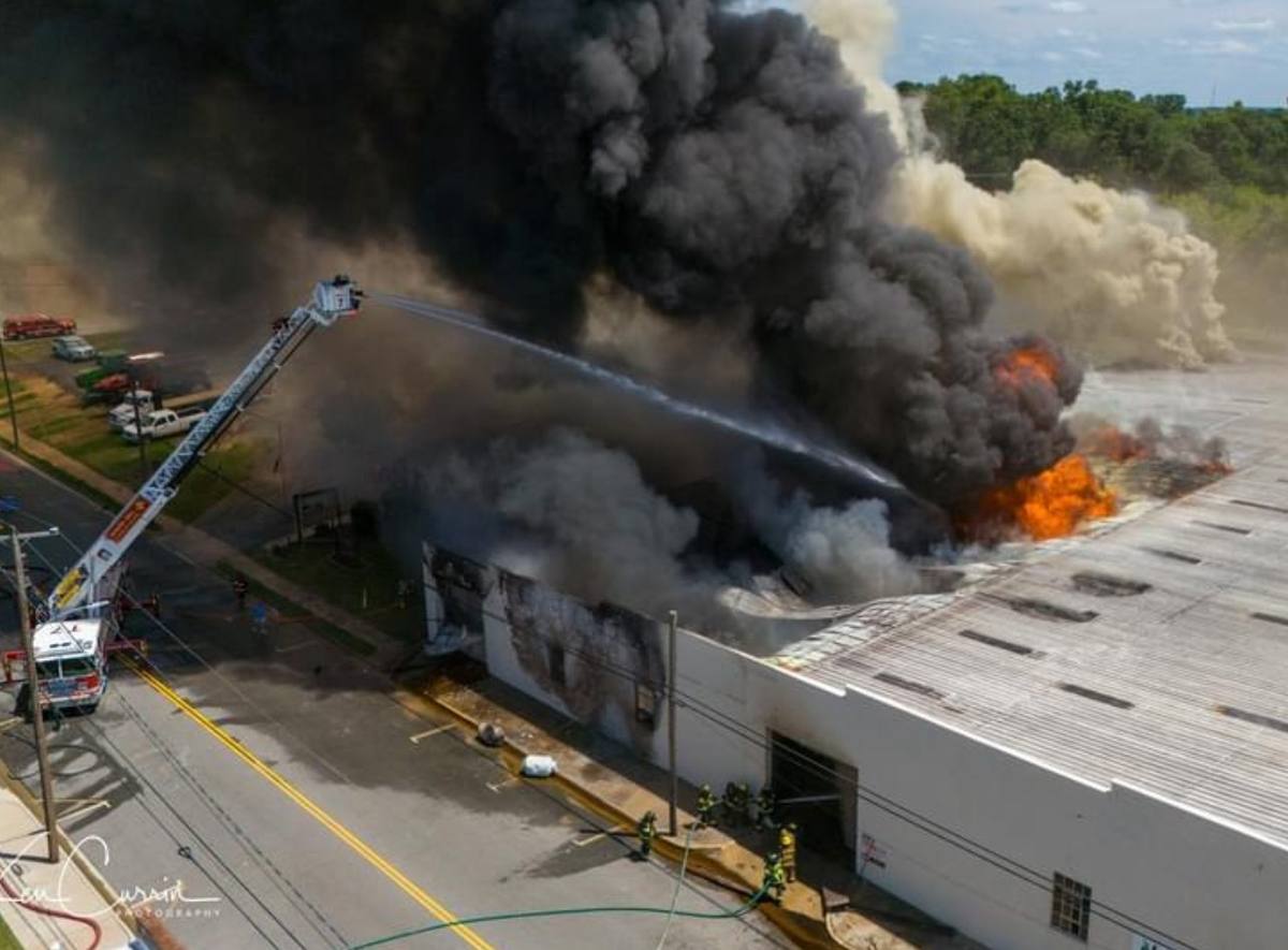 Aerial view of a commercial building fire with ladder streams working the roof line