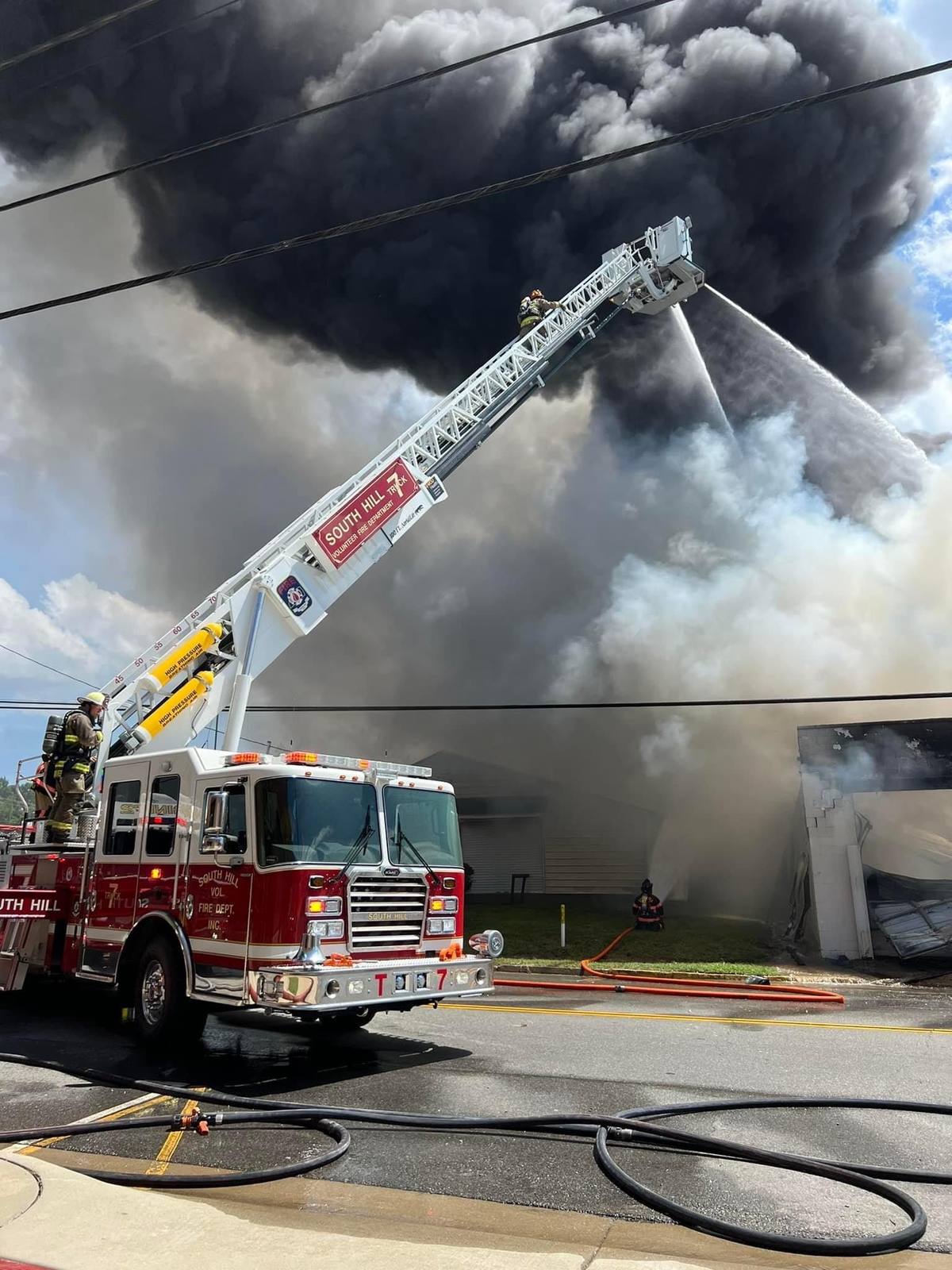 Aerial ladder flowing into heavy black smoke at a commercial fire, ground level view