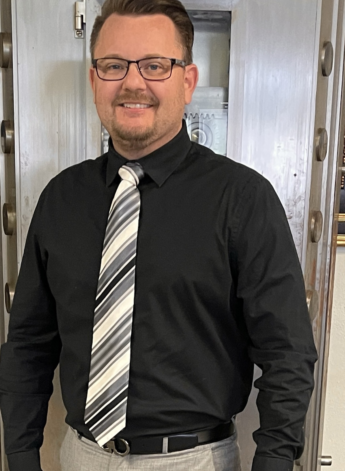 Derek Hazelwood, licensed in property and casualty and in life and health, standing in front of an open bank vault door